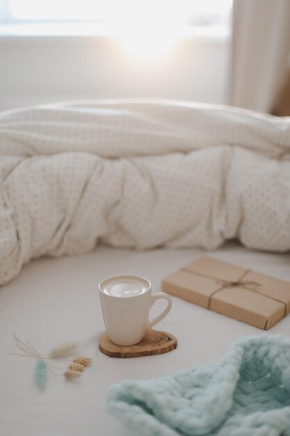 Light cozy bedroom Cup of aromatic coffee book and warm plaid on bed with soft blanket indoors top view