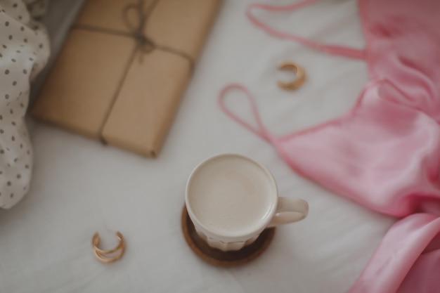 Light cozy bedroom Cup of aromatic coffee book and warm plaid on bed with soft blanket indoors top view