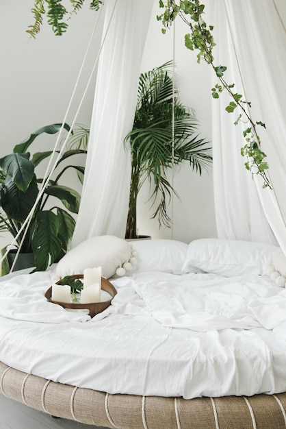 Light cozy bedroom made in white colors with round canopy bed. Modern cozy bedroom with round canopy bed and green tropical plants. Lazy morning at home and perfect place for relaxation concept.