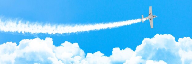 Light engine airplane with a trace of white smoke fly on cumulus clouds in summer, panorama.