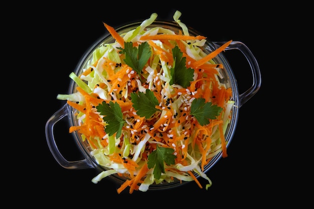 Light fresh salad of young cabbage and carrots in a glass bowl isolated on black background Top view with copy space