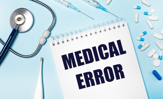 On a light gray background, a stethoscope, an electronic thermometer, pills, syringes and a notebook with the text MEDICAL ERROR. Medical concept.