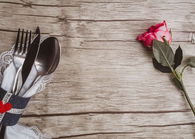 Light pastel colored tableware set vintage silverware on napkin and delicate pink rose on rustic shabby wooden background with copy space Top view