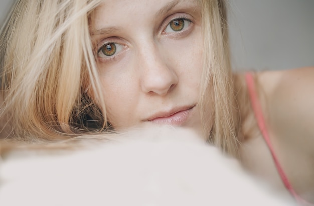 Light portrait of sad or tired blonde woman with green and brown eyes looking at camera