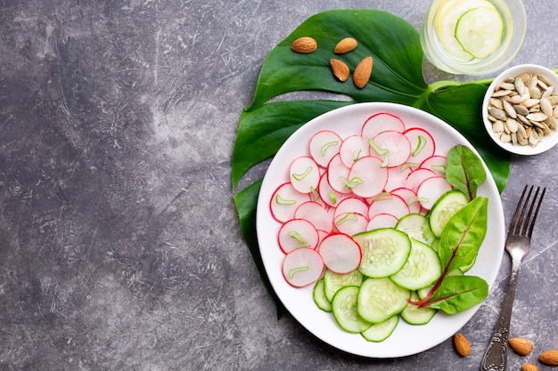 Light salad of radish with cucumber, detox drink with lemon, almonds and pumpkin seeds on a gray surface. Healthy eating concept.