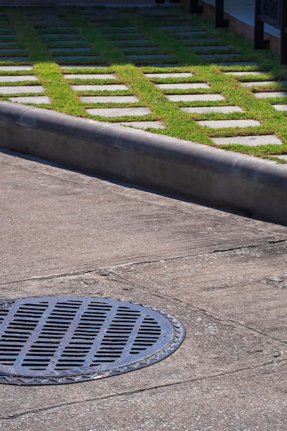 Light and shadow on surface of manhole cover on street with sidewalk decorative in vertical frame