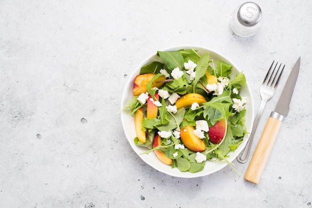 A light summer salad of rucolla peaches and cheese spoon and knife on a light gray background