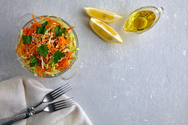 Light summer vegetable salad of cabbage carrots and sesame seeds dressed with lemon and olive oil Coleslaw salad garnished with parsley surrounded by ingredients on light concrete table