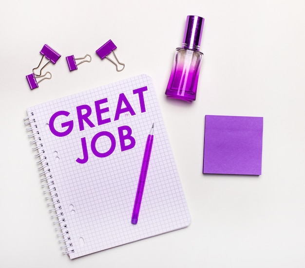 On a light surface - a lilac gift, perfume, lilac business accessories and a notebook with a lilac inscription GREAT JOB. Flat lay. Womens business concept