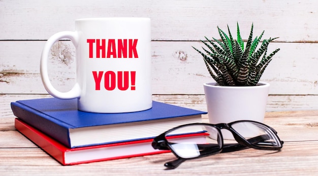 On a light table are notepads a potted plant blackframed glasses and a white cup with the text THANK YOU