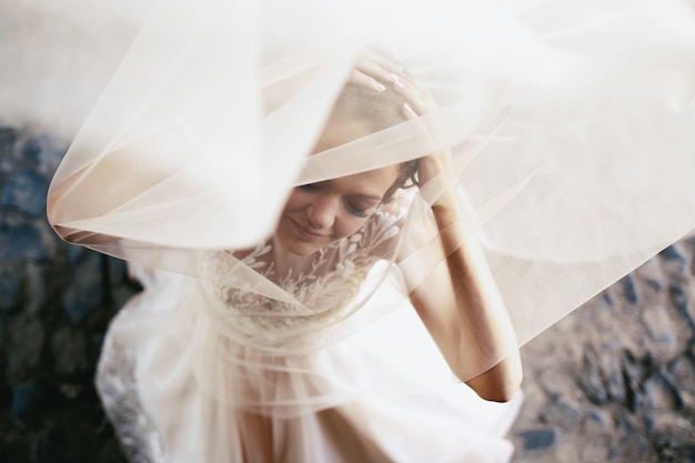 Light veil covers dreamy bride posing on the pavement