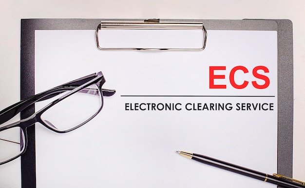 On a light wooden background glasses a pen and a sheet of paper with the text ECS Electronic Clearing Service Business concept