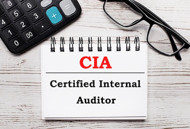 On a light wooden table calculator glasses and a blank notepad with the text CIA Certified Internal Auditor Business concept