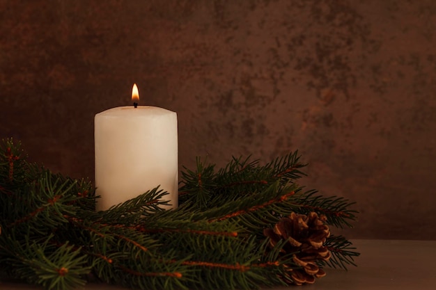 Lighted Christmas candle on a dark background near the Christmas tree branches