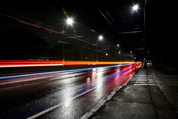 Lights of cars at night. Street lights. Night city. Long-exposure photograph night road. Colored bands of light on the road. Wet road after rain.