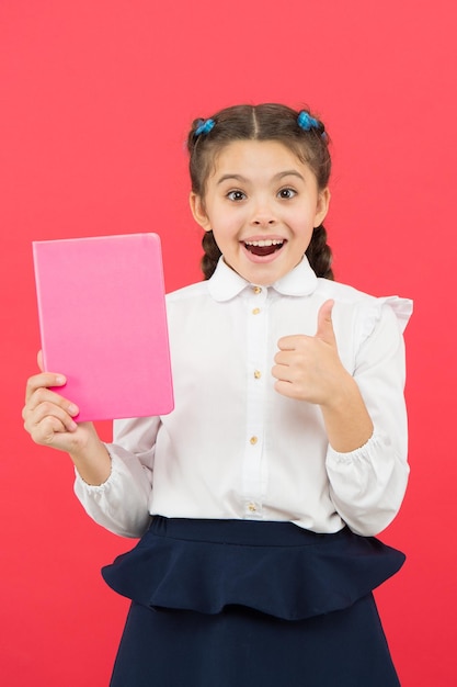 Liking her idea. Happy schoolgirl got main idea of book. Adorable little girl with book showing ok sign to bright idea. Small cute child smiling of genius idea, copy space.