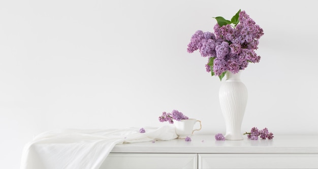 Lilac flowers in white vase on background white wall