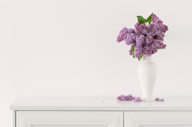 Lilac flowers in white vase on background white wall