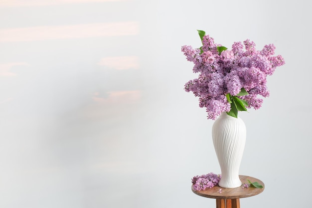 lilac flowers in white vase on background white wall