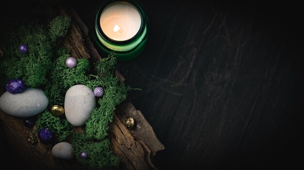 Lilac golden stone lies in the bark of a tree with green moss gray stones and a burning candle on a black