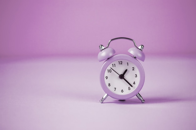 Lilac small alarm clock on a lilac background.