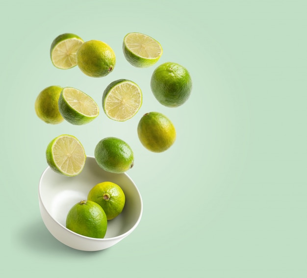 Limes flying in white bowl on green background