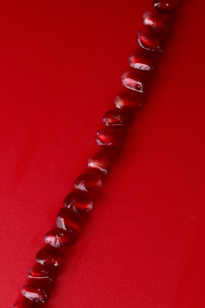 Line of ruby ripe fresh juicy pomegranate seeds close up isolated on red background with copy space