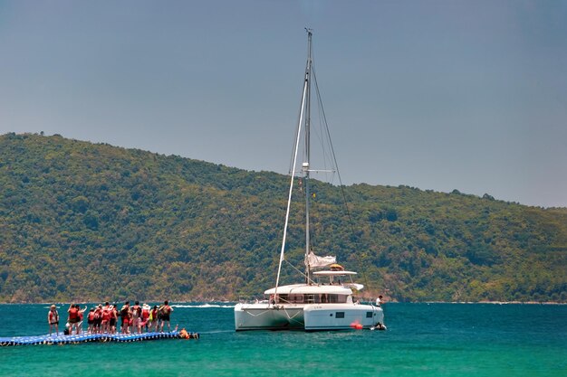 The line of vacationers stands at the pier waiting for boarding the yacht