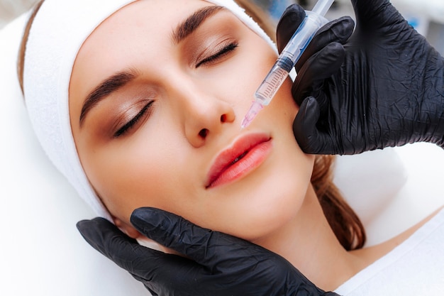 Lip augmentation procedure with hyaluronic acid. The beautician pierces the lips with a needle. Subcutaneous injection.