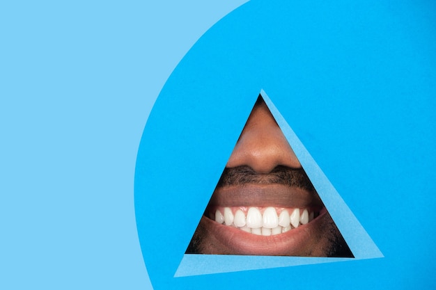 Lips of africanamerican man peeking throught triangle in blue background