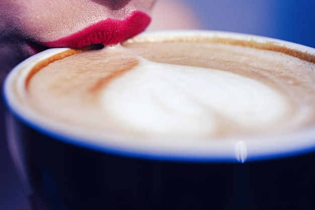 Lips girl touch the cup with coffee Coffee mug with heart shape on the froth Closeup of cappuccino s