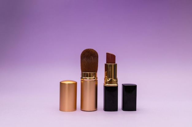 Lipstick and powder brush on purple background subject