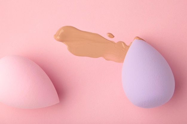 Liquid beige makeup foundation with sponges on pink background