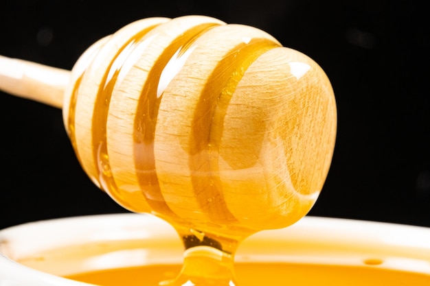 Liquid natural bee honey in a white ceramic bowl with a wooden spoon