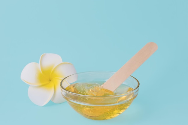 Liquid yellow sugar paste wooden spatula and flower on a blue background Sugaring Epilation Beauty