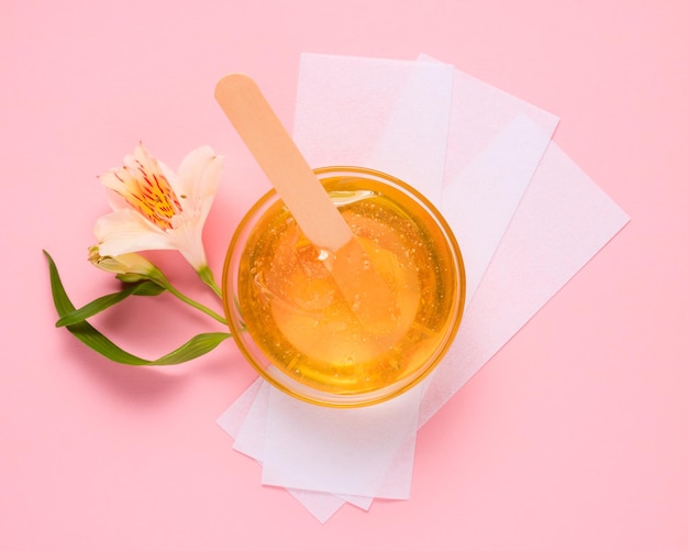 Liquid yellow sugar paste wooden spatula flower and depilatory strips on a pink background