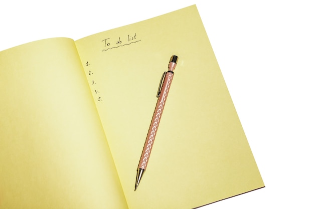 To do list in yellow notebook with pink pen isolated on white. Working place and planning concept, top view.