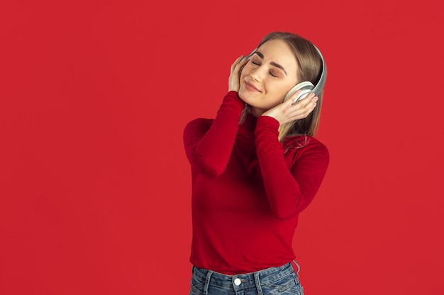 Listen to music. Monochrome portrait of young caucasian blonde woman isolated on red wall.