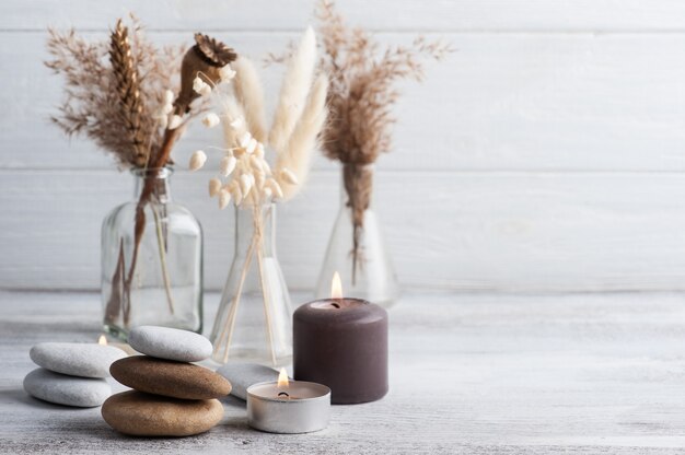 Lit aroma candles and dry flowers on rustic background. Spa arrangement in monochrome style