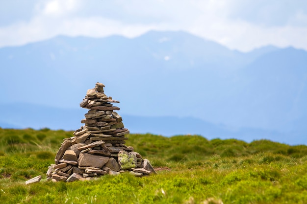 Lit by bright summer sun uneven mountain stones stacked and balanced like pyramid pile on green grassy valley on light white blue copy space sky background. Tourism. Traveling and landmark concept.