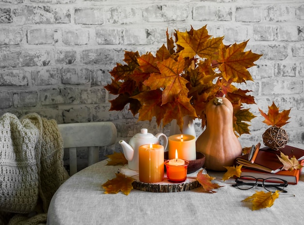 Lit candles dry maple leaves pumpkin stack of books autumn still life interior decoration house Cozy home concept