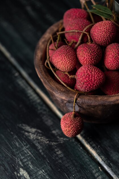 Litchi is placed in a wooden plate, peeled or unopened, on a dark wood grain table