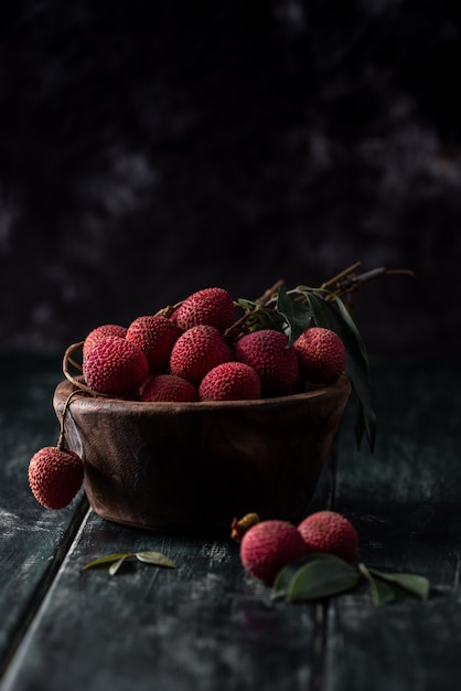 Litchi is placed in a wooden plate, peeled or unopened, on a dark wood grain table