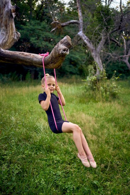 Photo a little 5yearold gymnast in a black minimalist jumpsuit swings on a gymnastic rope on a tree