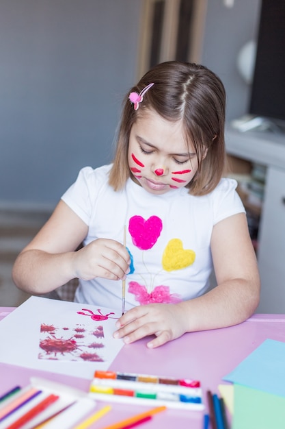 Little adorable cute cheerful joyful girl drawing alone at home during vacation or quarantine witn mouse on her face. Childhood home activity at home, art for kids