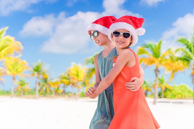 Little adorable girls in Santa hats during beach vacation have fun together