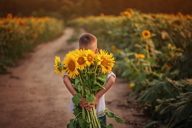 Photo little adorable kid boy holding bouquet of sunflowers in summer day.