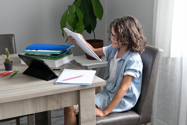 Little adorable school boy with eyeglasses studying online from home kid using digital tablet