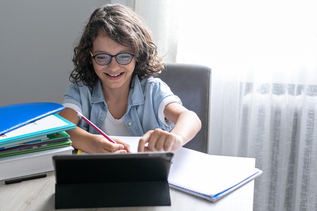 Little adorable school boy with eyeglasses studying online from home kid using digital tablet