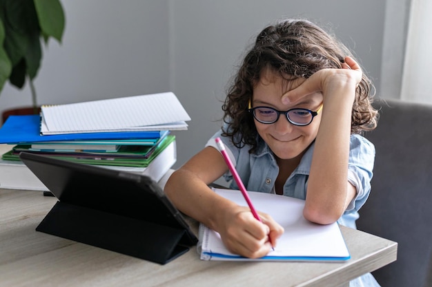 Little adorable school boy with eyeglasses studying online from home kid using digital tablet